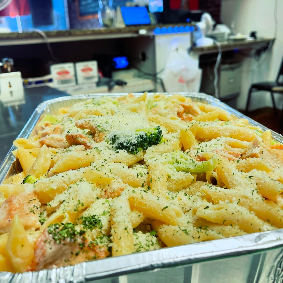 A large foil tray of Anna's Kitchen penne pasta with chicken, broccoli, and parmesan cheese.